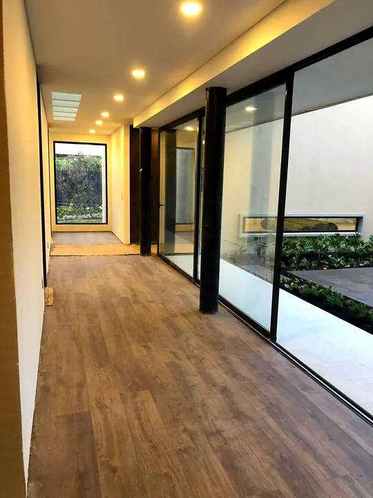 Corredor interior con piso en madera y ventanales hacia el patio